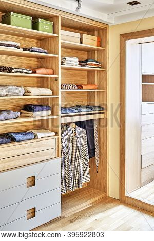 Modern Wardrobe With Clothes Hanging On Slide Out Racks And Folded On The Shelves. Modern Furniture