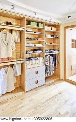 Modern Wardrobe With Clothes Hanging On Slide Out Racks And Folded On The Shelves. Modern Furniture