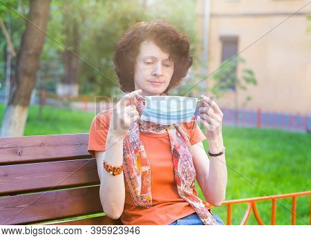 Portrait Of Red Woman Sitting On The Street Bench With Protective Mask As Protection Against Infecti