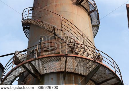 Remains Of An Old Factory. The Round Steel Chimney And The Steel Construction Of The Building Are Cl