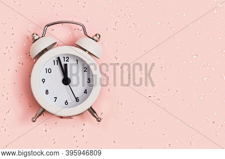 White Alarm Clock Shows About Twelve Oclock On Pink Paper Background Covered With Sequins With Copy 