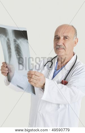 Portrait of serious senior male doctor holding medical radiograph over gray background