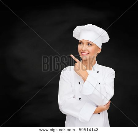 cooking, advertisement and food concept - smiling female chef, cook or baker pointing finger to something