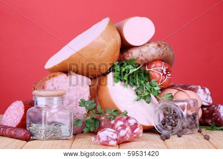 Lot of different sausages on wooden table on red background