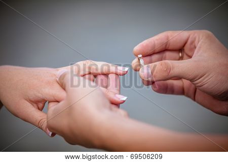 Man placing a diamond engagement ring on the finger of his fiance. Shallow depth of field with focus on the ring