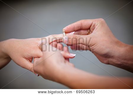 Man placing a diamond engagement ring on the finger of his fiance. Shallow depth of field with focus on the ring