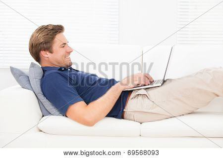 Smiling Man Using Laptop On Sofa
