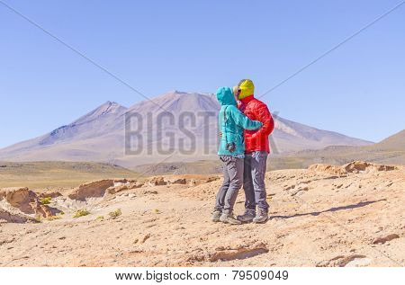 Bolivia, Antiplano - couple of tourists kiss in front of volcano Ollague
