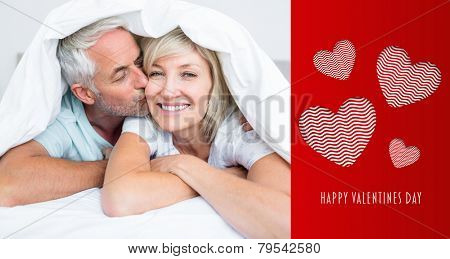 Closeup of mature man kissing womans cheek in bed against cute valentines message