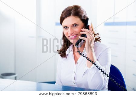 Doctors nurse with telephone in front desk making appointment with patient