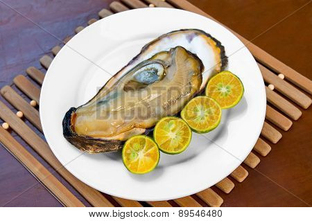 Opened Fresh Oyster In A White Plate With Lime On A Wooden Table