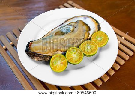 Opened Fresh Oyster In A White Plate With Lime On A Wooden Table