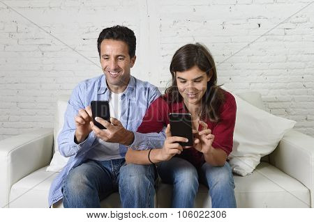Young Attractive Couple Of Man And Woman Together At Home Couch With Arms Interlaced Using Mobile Ph