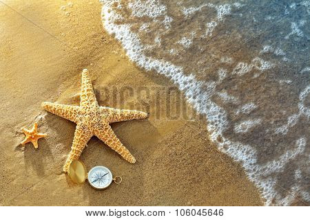 Compass with sea stars on sand beach background