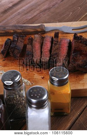 fresh roast red beef meat fillet mignon cutted on wooden plate with vintage fork many different kinds of dry spice over table