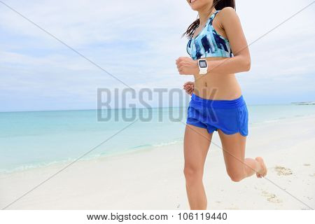 Runner running wearing smartwatch. Closeup of fitness woman wearing blue shorts and sports bra training cardio on beach using app on smart watch to monitor heart rate and speed.