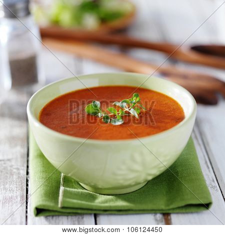 tomato soup in green bowl with herb garnish on rustic table
