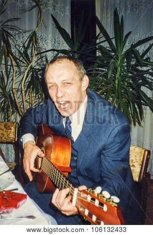 LODZ, POLAND, CIRCA 1990: Vintage photo of man playing guitar and singing during a family party