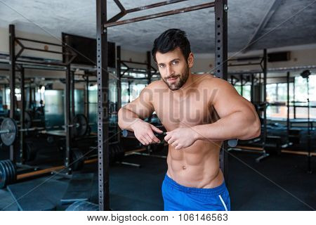 Portrait of a mucular male bodybuilder resting near parallel bars in fitness gym and looking at camera