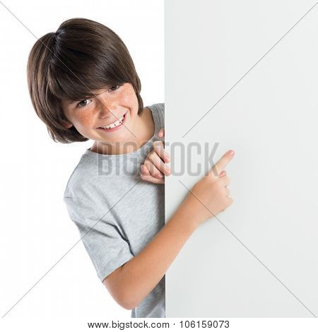 Portrait of smiling little boy pointing at blank placard isolated white background. Happy boy standing behind at blank grey poster indicate and looking at camera.
