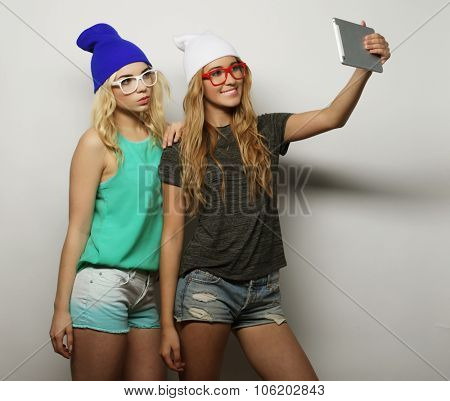two hipster girls friends taking selfie with digital tablet, studio shot over gray vackground