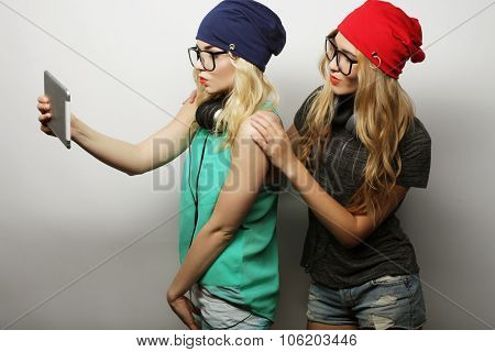 two hipster girls friends taking selfie with digital tablet, studio shot over gray vackground
