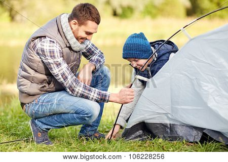 camping, tourism, hike, family and people concept - happy father and son setting up tent outdoors