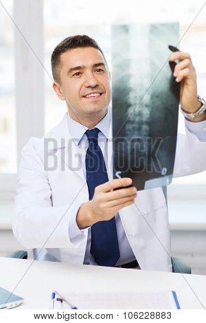 healthcare, rontgen, people and medicine concept - smiling male doctor in white coat looking at x-ray in medical office