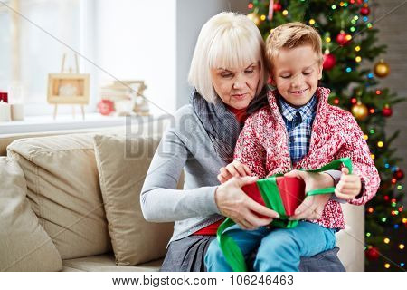 Mature woman helping her grandson untie gift-box on Christmas eve