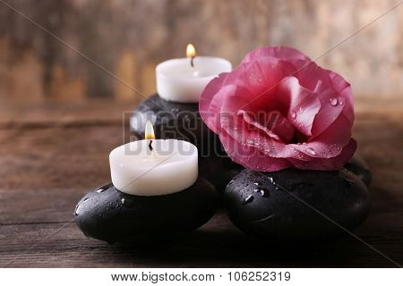 Alight candles, pebbles and fresh aroma flower composition on wooden background
