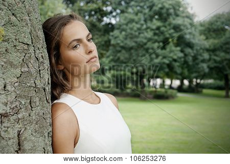 sad young woman leaning against tree