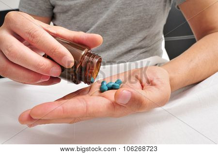 a young caucasian man in pajamas in bed about to take some blue pills from a brown bottle