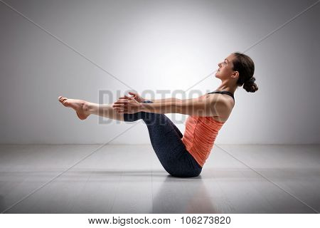 Beautiful sporty fit yogini woman practices yoga asana Paripurna navasana - boat pose beginner variation
