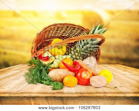 The basket with fruits and vegeetables on wooden desk and autumn field on background