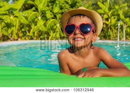Boy in heart-shaped sunglasses on green airbed