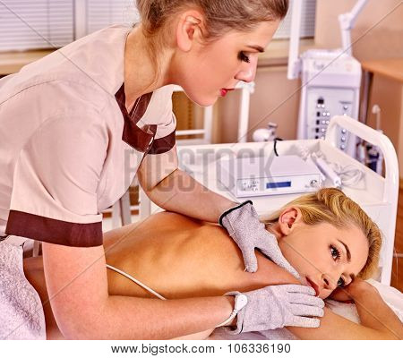 Young white  woman  receiving electric massage at beauty salon. Beautician wearing electricity gloves. In room is device for hardware cosmetology. 