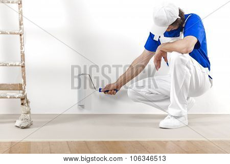 Painter Man At Work With Paintroller Painting A White Wall.