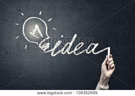 Human hand darwing light bulb as idea concept with chalk