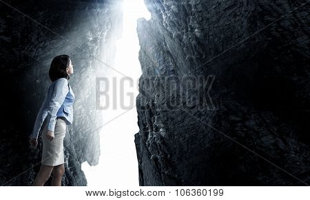 Young businesswoman making fists and reaching light in wall crack