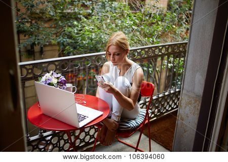 Female student chatting on mobile phone while rest after work on net-book