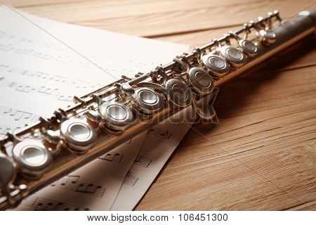 Silver flute with music notes on wooden table close up