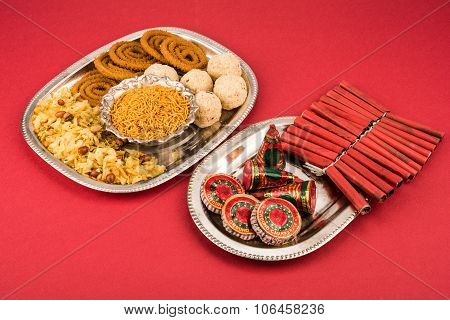Diwali snacks with Diwali fire crackers in silver plate isolated on red background