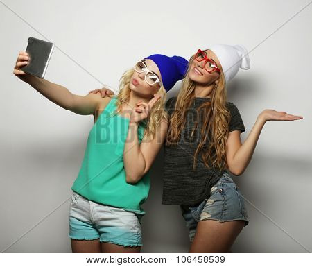 two hipster girls friends taking selfie with digital tablet, studio shot over gray vackground