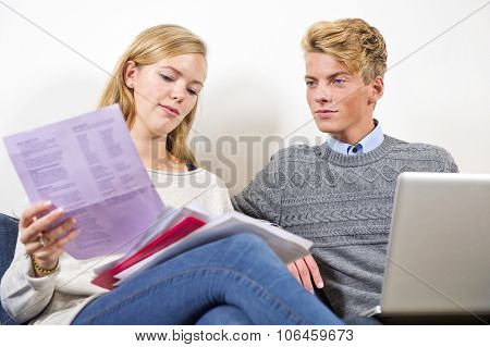 Young couple sitting next to eachother, going through bills, invoices and other paperwork, balancing their checkbook on a laptop