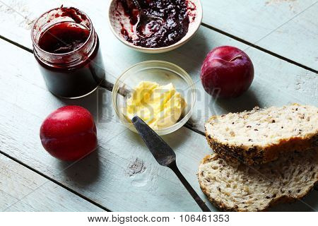 Tasty jam in the jar and bowl, butter, fresh bread, plums and tablet on blue wooden background