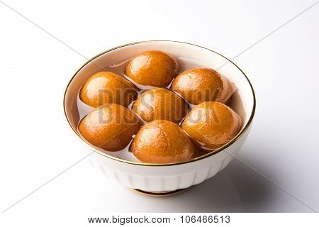 indian sweet gulab jamun dipped in a sweet syrup in white ceramic bowl on red wooden background, iso