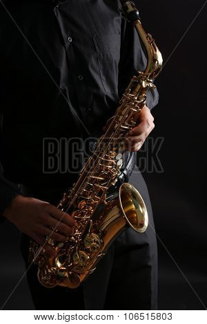 Musician in black shirt with sax on dark background, close up