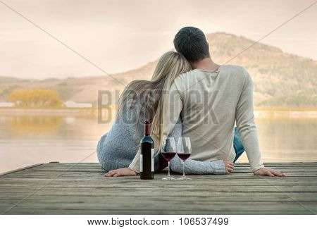 Romantic Couple sitting on the pier with red wine.