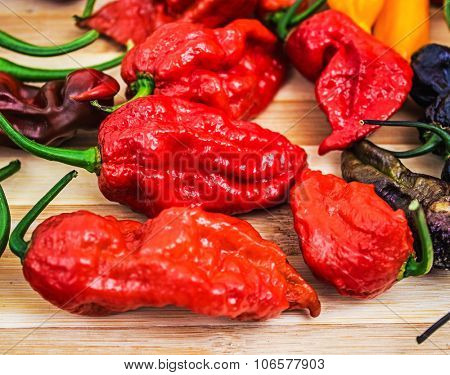 Various very hot chili peppers on wooden table, habanero, scorpion, moruga, jolokia