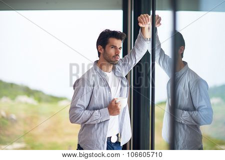 relaxed young man drink first morning coffee at modern home indoors at rainy window drops window